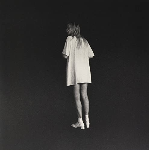 Person from behind wearing a light dress, dark background.
