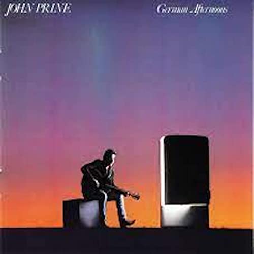 John Prine sitting on a box playing guitar against a sunset sky.