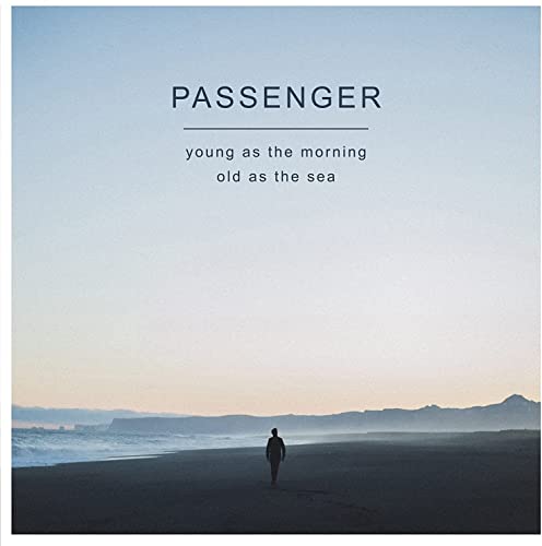 Album cover: lone figure on a beach with ocean and mountains.