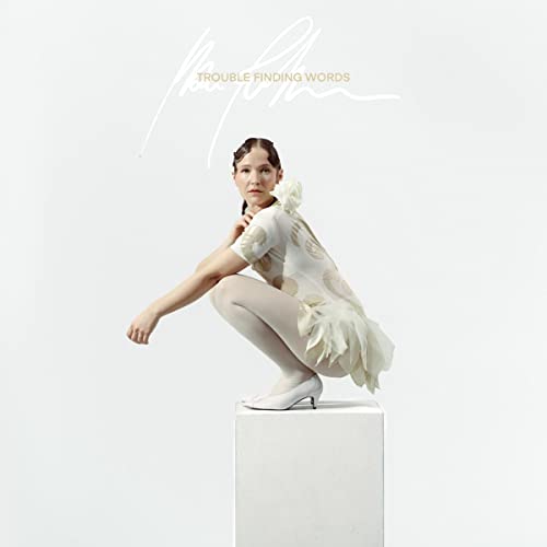 Album cover: woman in white dress crouching on a white cube.