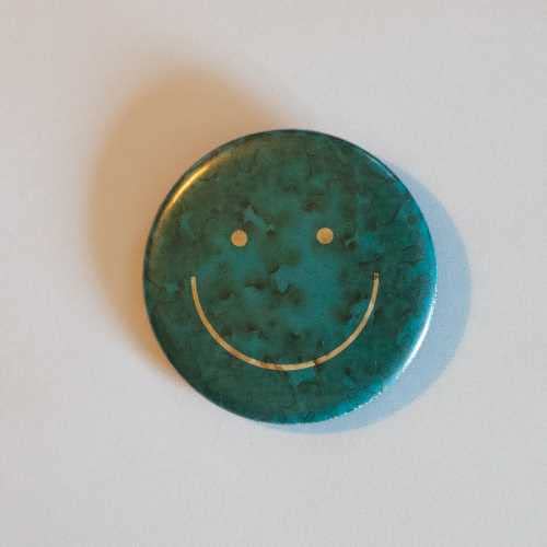 Teal CD case with a gold smiley face, casting a soft shadow.