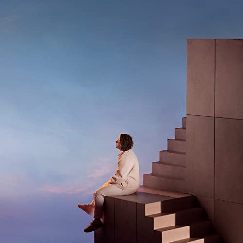 Man in light sweater sits on concrete stairs, looking upwards.