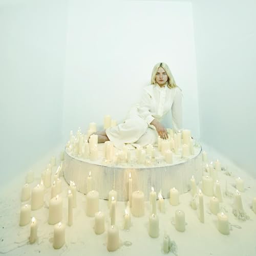 Woman in white clothing sitting on a platform surrounded by many lit white candles.