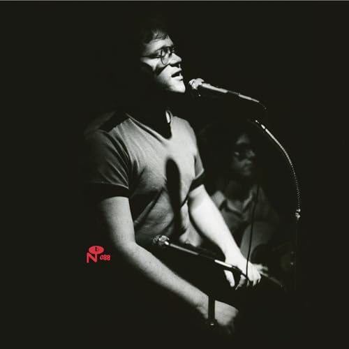 Black and white photo of a man singing into a microphone onstage.