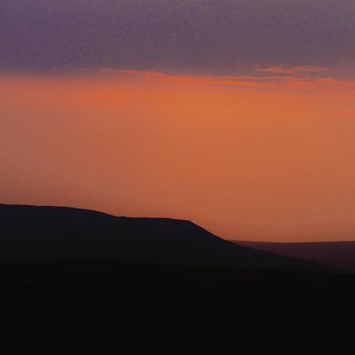Sunset over dark, silhouetted hills with orange and purple sky.