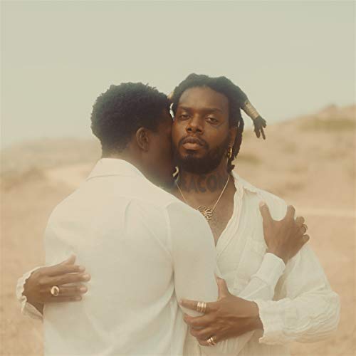 Two Black men embrace, facing the viewer, in a desert landscape.