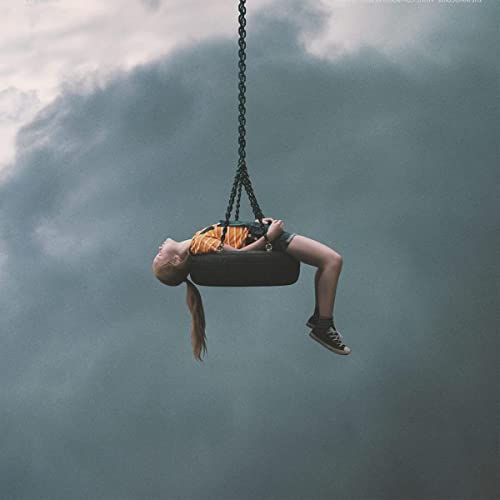 Girl lying on a tire swing against a cloudy, grey sky.