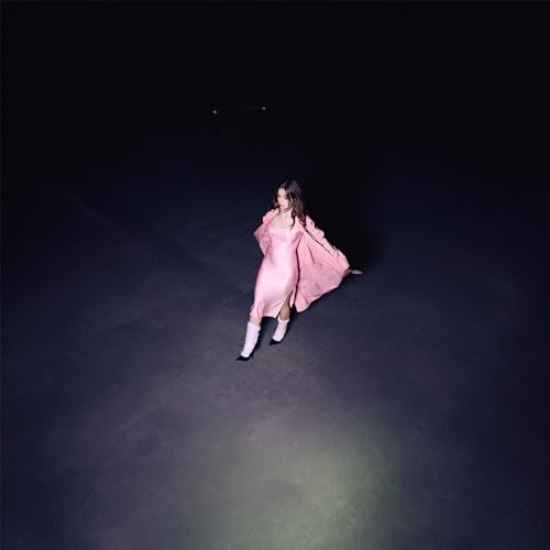Woman in pink dress and boots, standing in a dark space.