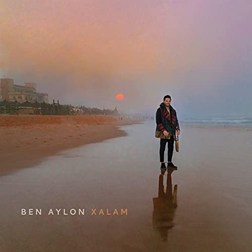Man with a stringed instrument on a beach at sunset.