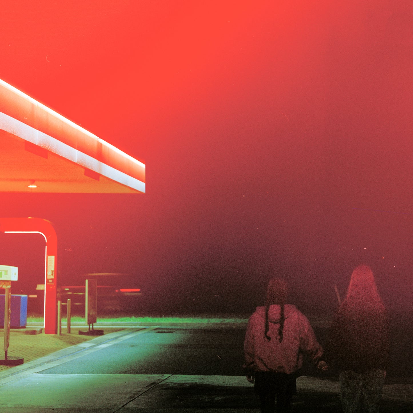 Red-toned image of two figures walking away from a brightly lit building.