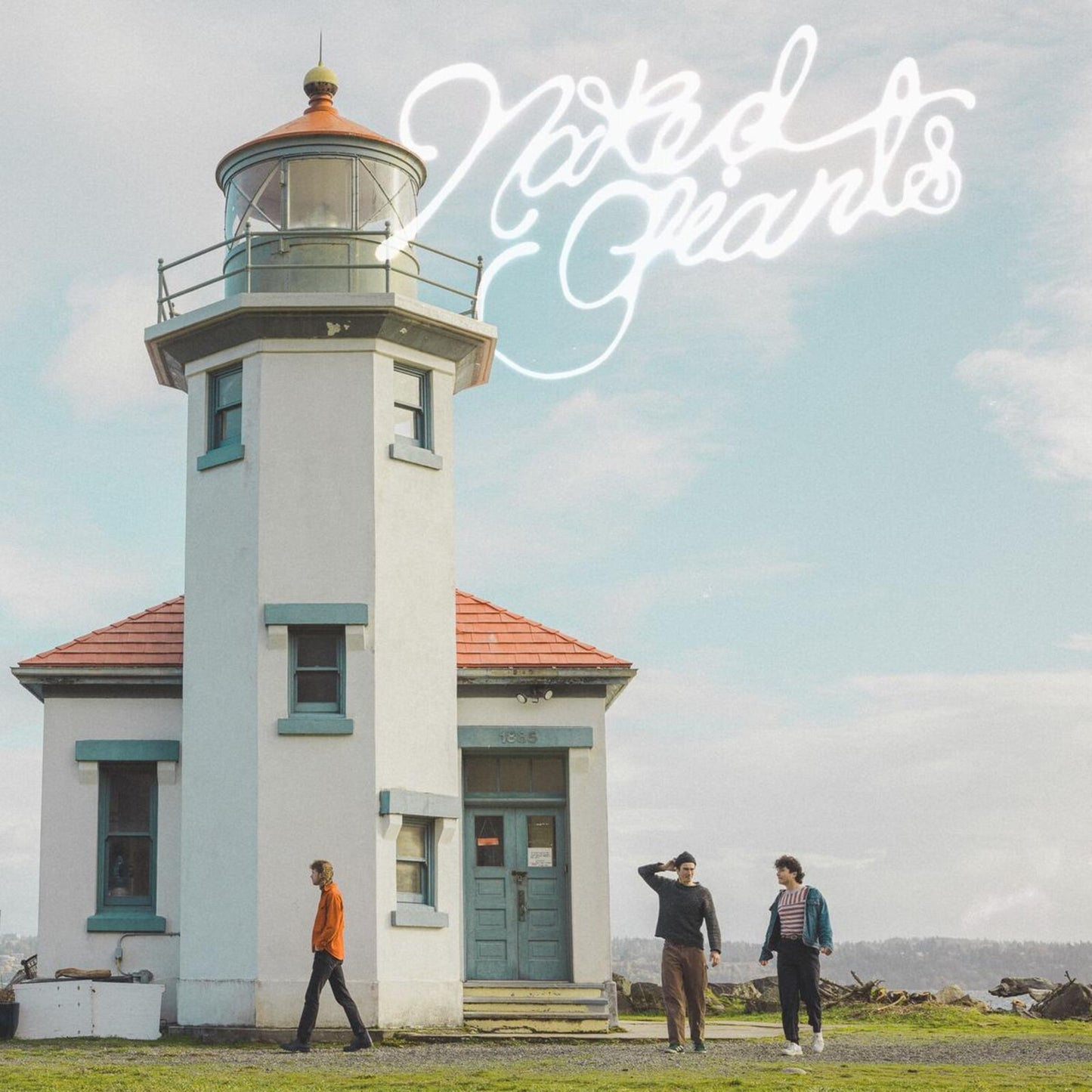 Lighthouse with three people standing in front on a grassy field.