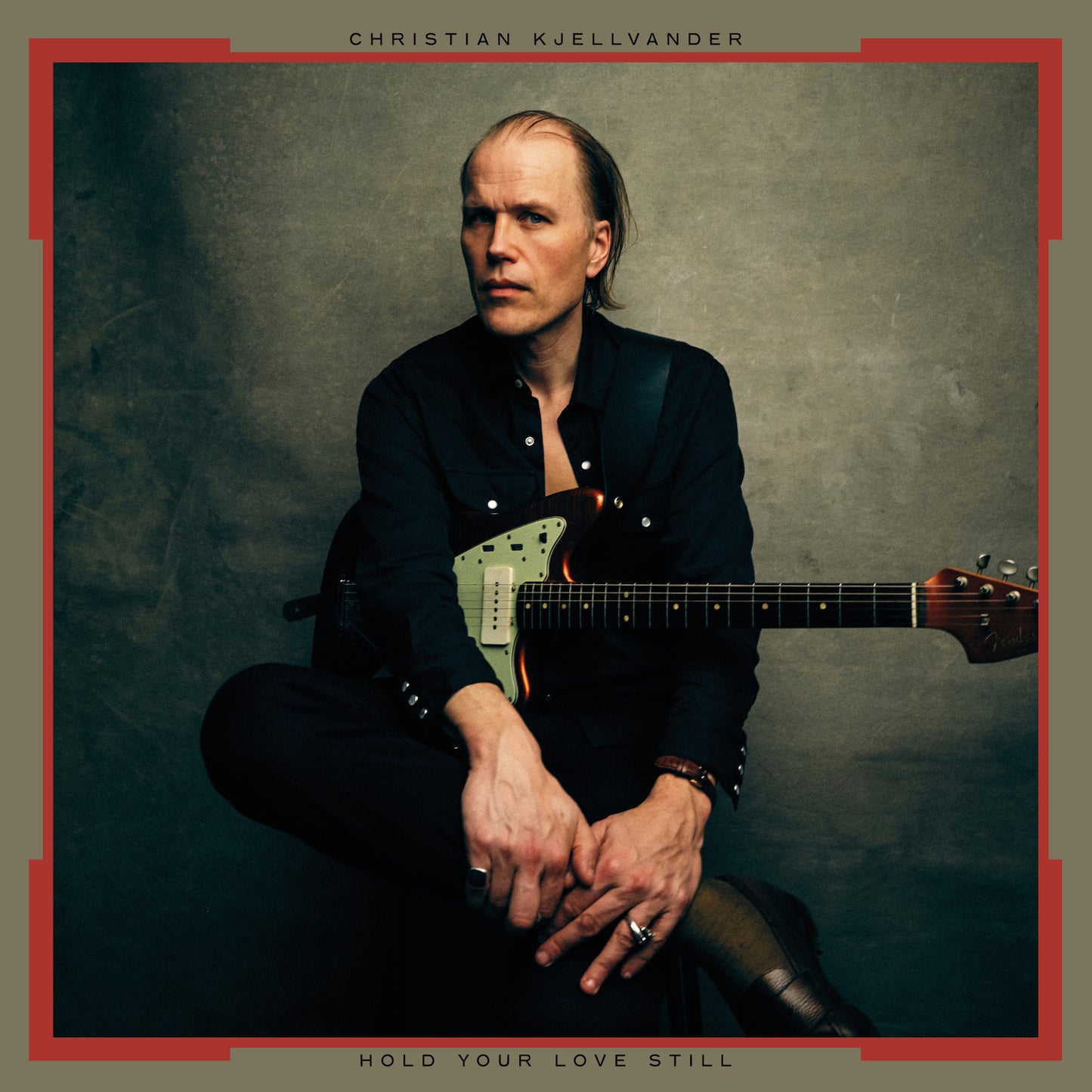Man with a guitar sitting against a textured gray background.