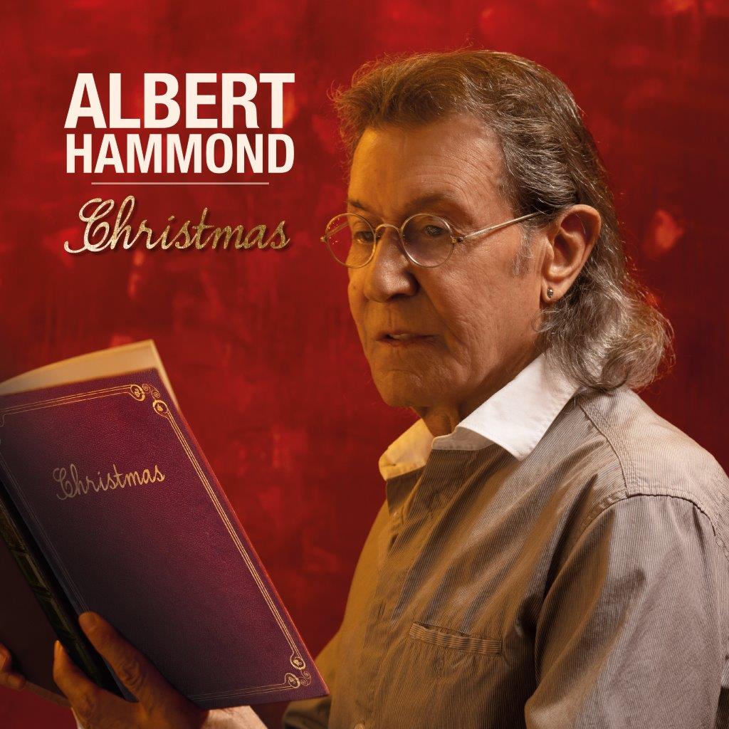 Albert Hammond portrait holding a red book against a red background.