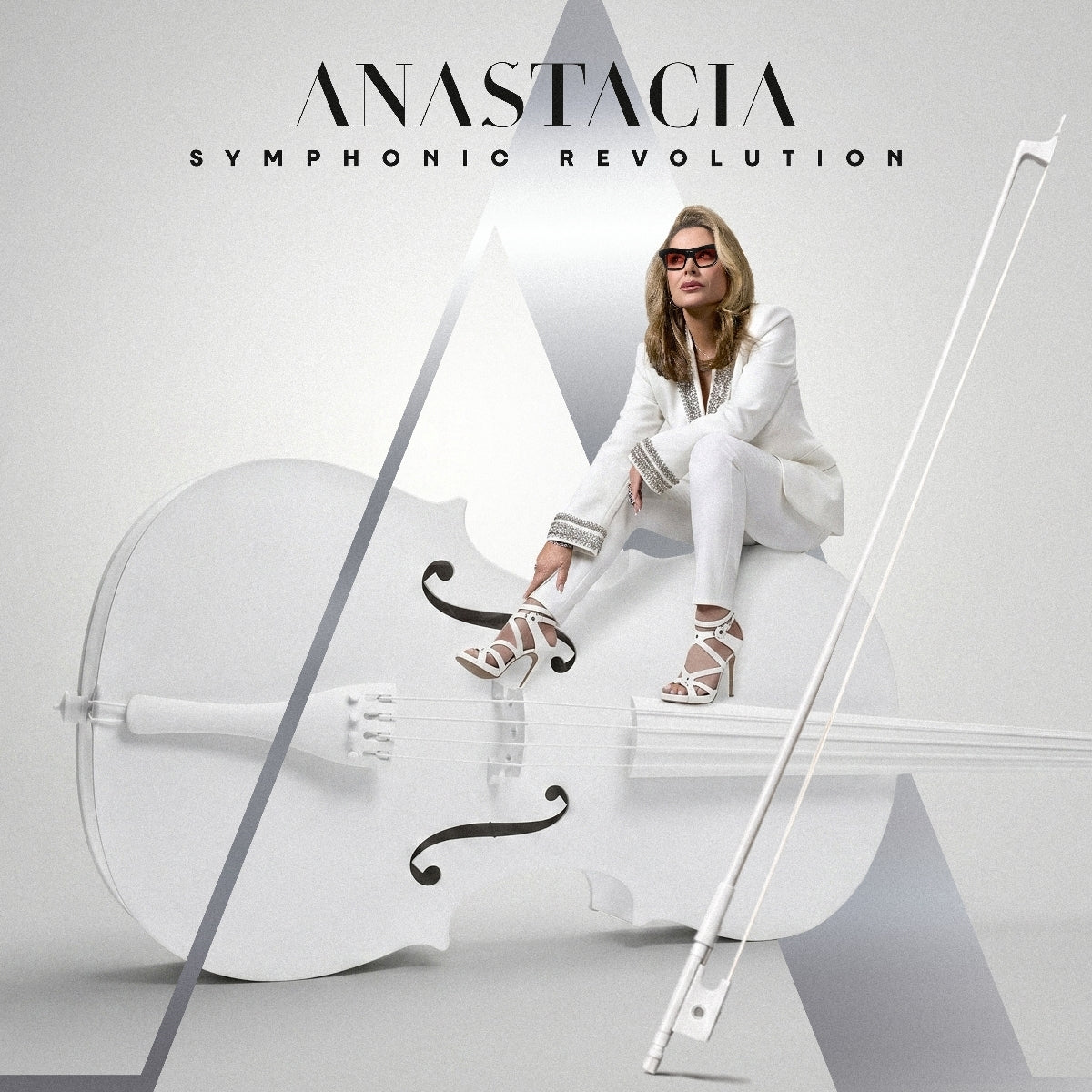 Anastacia sits with a large, white cello in a minimalist, grey setting.