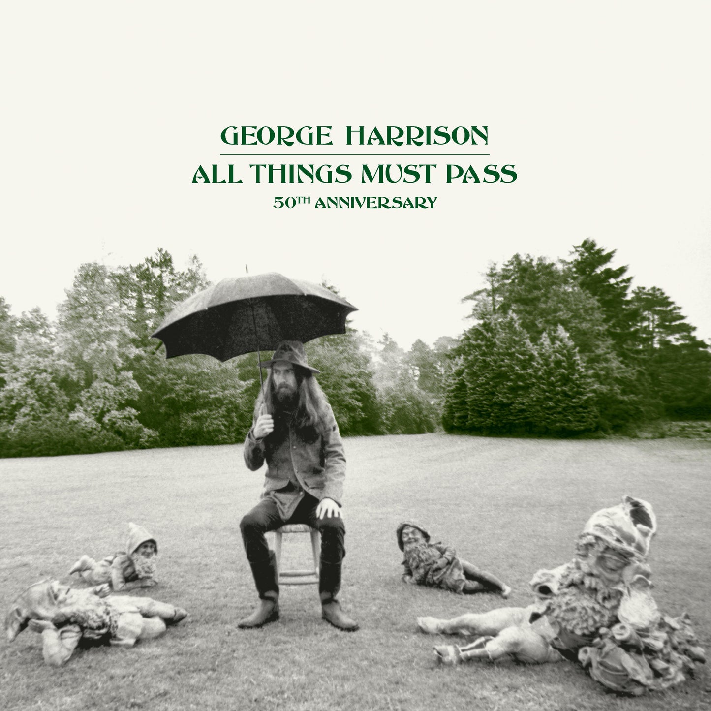 George Harrison sits on a stool under an umbrella surrounded by garden gnomes.