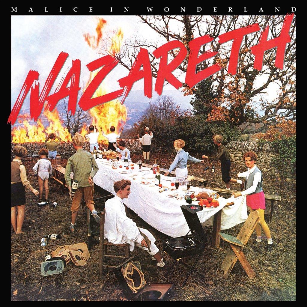 Children gather around a long outdoor banquet table with a bonfire burning in background.