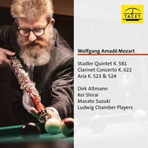 Bearded man in suit playing a clarinet like a pool cue on a table.
