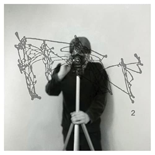 Black and white album cover featuring a person holding a camera with abstract lines.