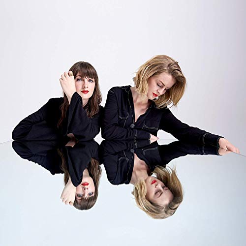Two women, Ward Thomas, reflected in a mirrored surface, wearing dark shirts.