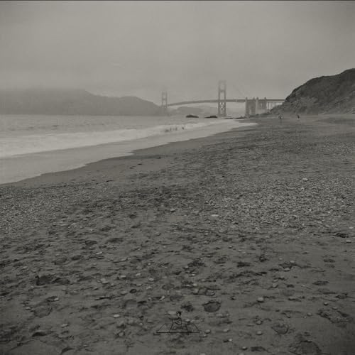 Black and white beach scene with the Golden Gate Bridge in the distance.