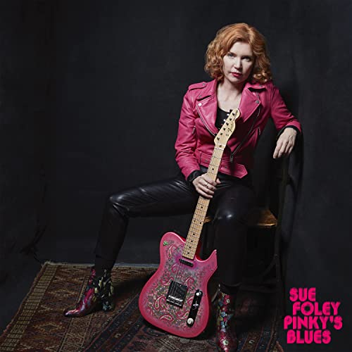 Sue Foley sits with a pink guitar, wearing a pink jacket.
