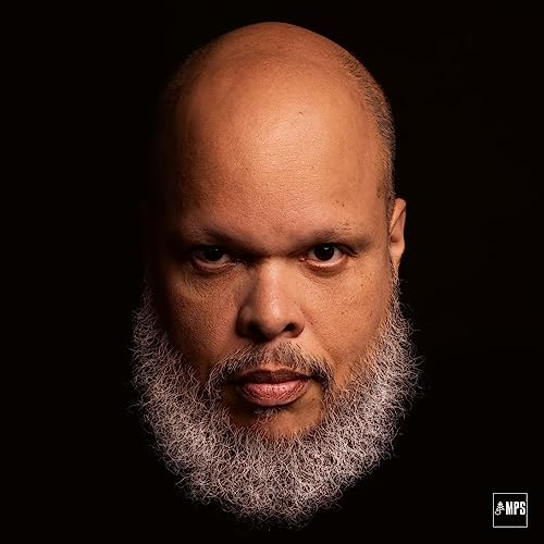 Close-up portrait of Motta,ed with a full beard, against a black background.