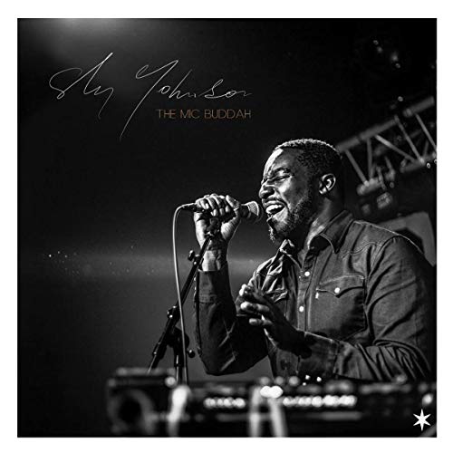 Black and white portrait of Sly Johnson performing with a microphone.