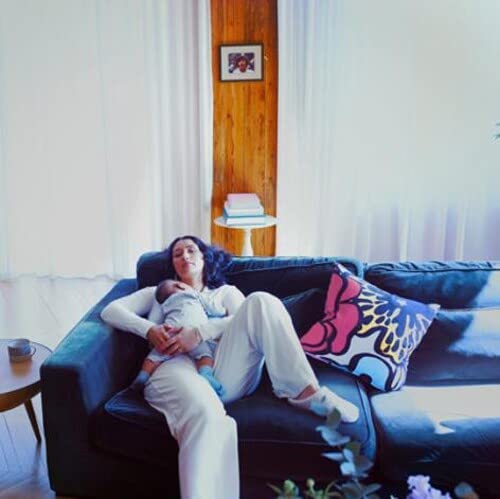 Woman holding a baby on a dark couch in a bright room.