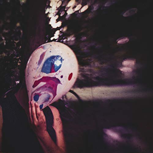 Person wearing a painted clown mask, dark and blurry background.
