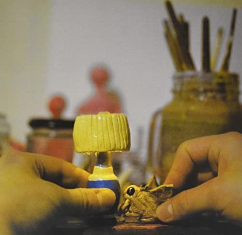 Hand holding a small, sculpted frog with a yellow lamp above.