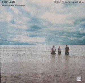 CD cover: three men stand in shallow water under a cloudy sky.