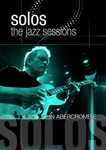 John Abercrombie playing a white electric guitar on a dark stage.