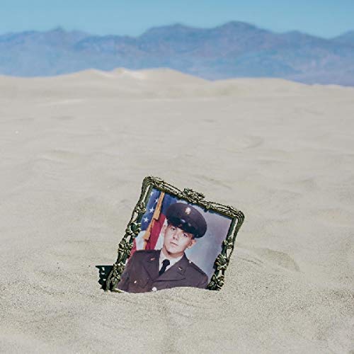Ornate framed portrait of a soldier partially buried in desert sand.