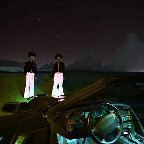 Two figures in pink suits stand by a car at night.