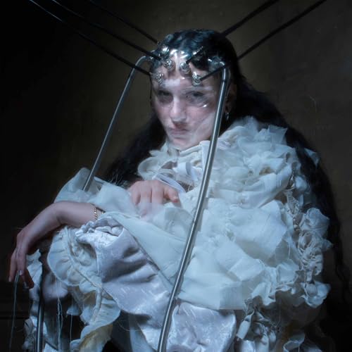 Woman with metallic headpiece and white ruffled garment, looking forward.
