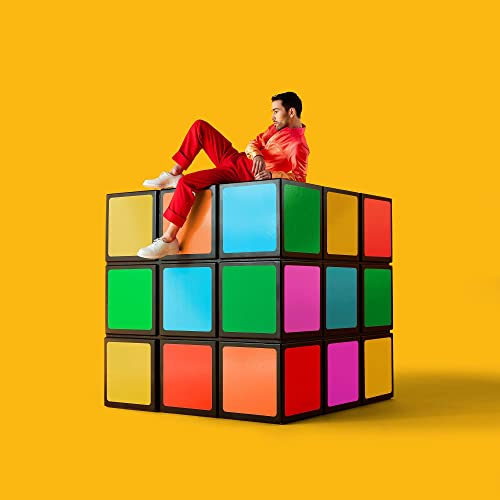 Man in red clothes sits atop a large, colorful Rubik's Cube.