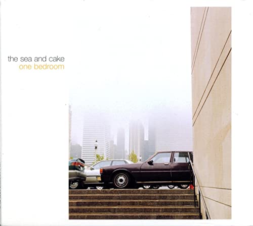 Album cover showing a dark car parked on stairs before a foggy city skyline.