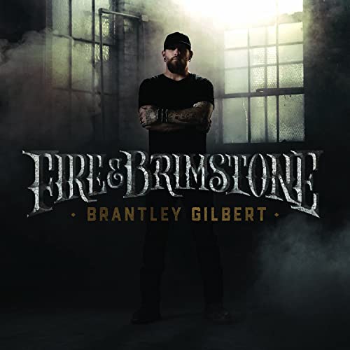 Brantley Gilbert stands with arms crossed in front of a window in smoky light.