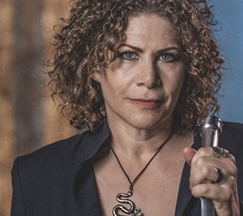 Dayna Kurtz portrait, curly hair, holding a microphone, wearing a blazer.