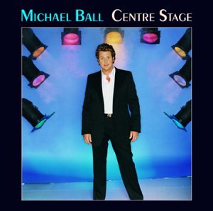 Michael Ball in a suit stands center stage under spotlights.