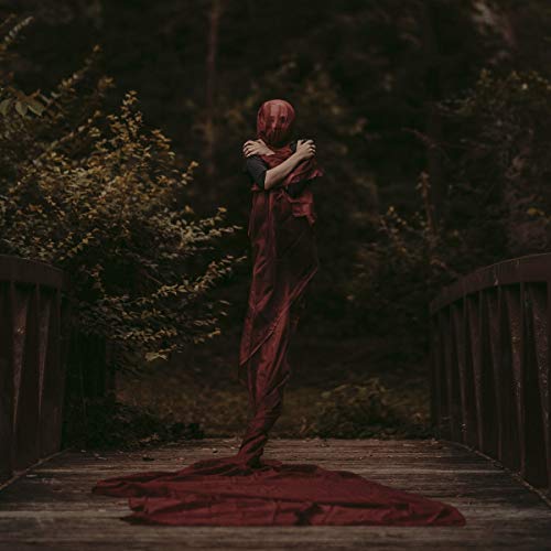 Figure in red fabric stands on a wooden bridge outdoors.