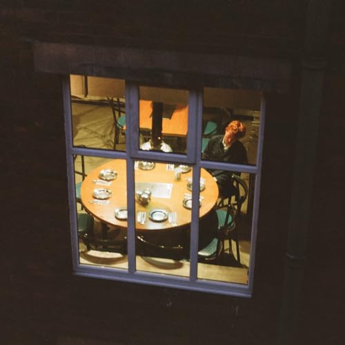 Person seated at a round table set for a meal, viewed through a window.