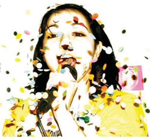 Woman singing into a microphone, surrounded by colorful confetti.
