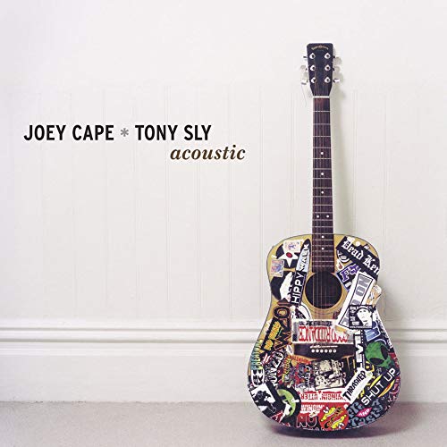 Sticker-covered acoustic guitar against a white paneled wall.