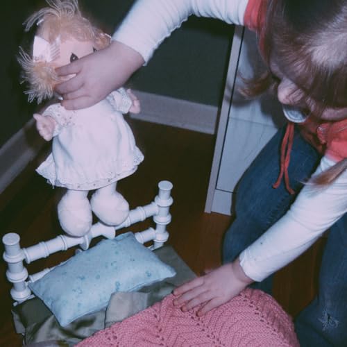 Child adjusting a vintage doll in a small white bed.