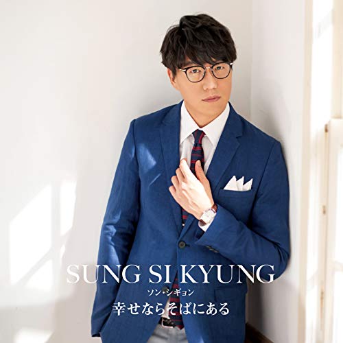 Sung Si-kyung wearing a blue blazer and glasses, leaning against a white wall.
