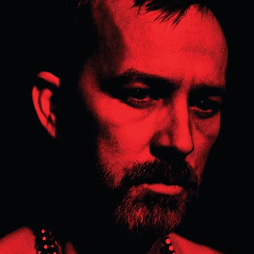 Red-toned portrait of a bearded man, close-up, looking downwards.