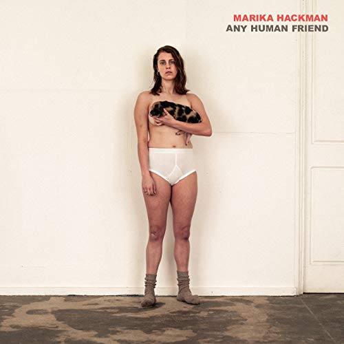 Woman in underwear holding a cat, standing against a white wall with a door.