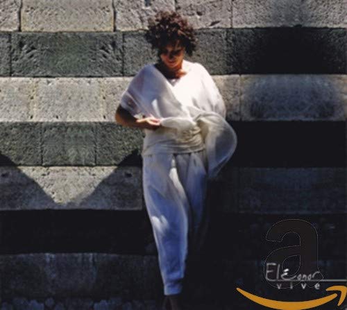 Woman in white clothing stands before a textured stone wall.