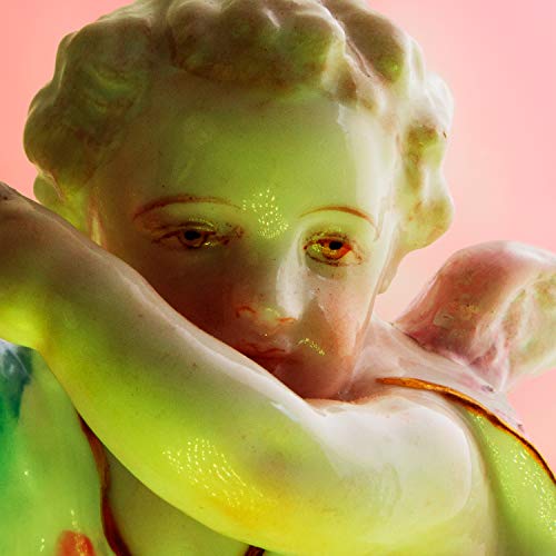 Close-up of a green and white porcelain cherub statue against pink.